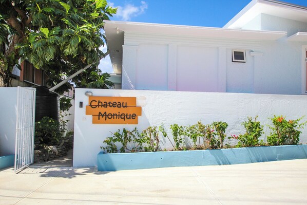 Un edificio blanco con un letrero que dice 'Chateau Monique' y una entrada con reja.