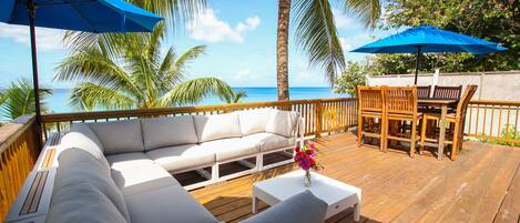 A wooden deck with a white sofa, wooden chairs, and two blue umbrellas.