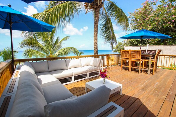 A wooden deck with a white sofa, wooden chairs, and two blue umbrellas. - Amazing Beachfront Paradise - Chateau Monique (Lower Carlton)
