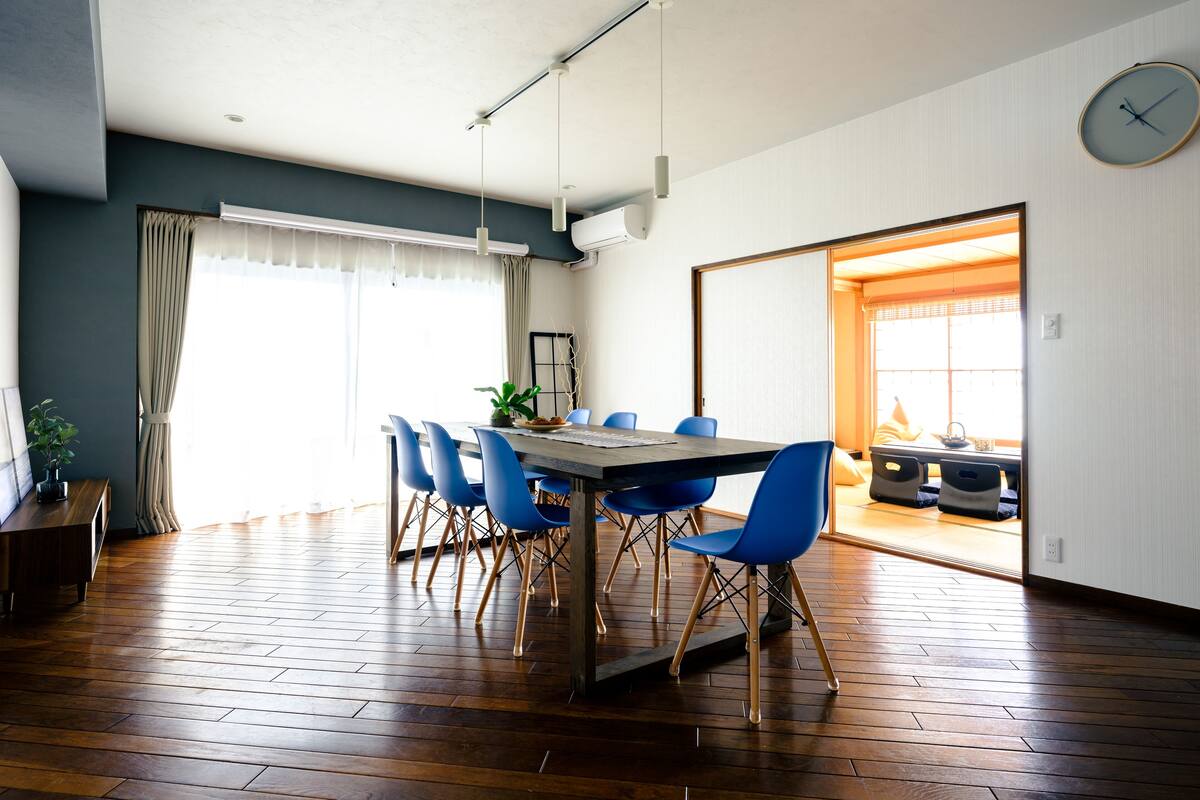 A dining area with a wooden table, blue chairs, and a clock on the wall.