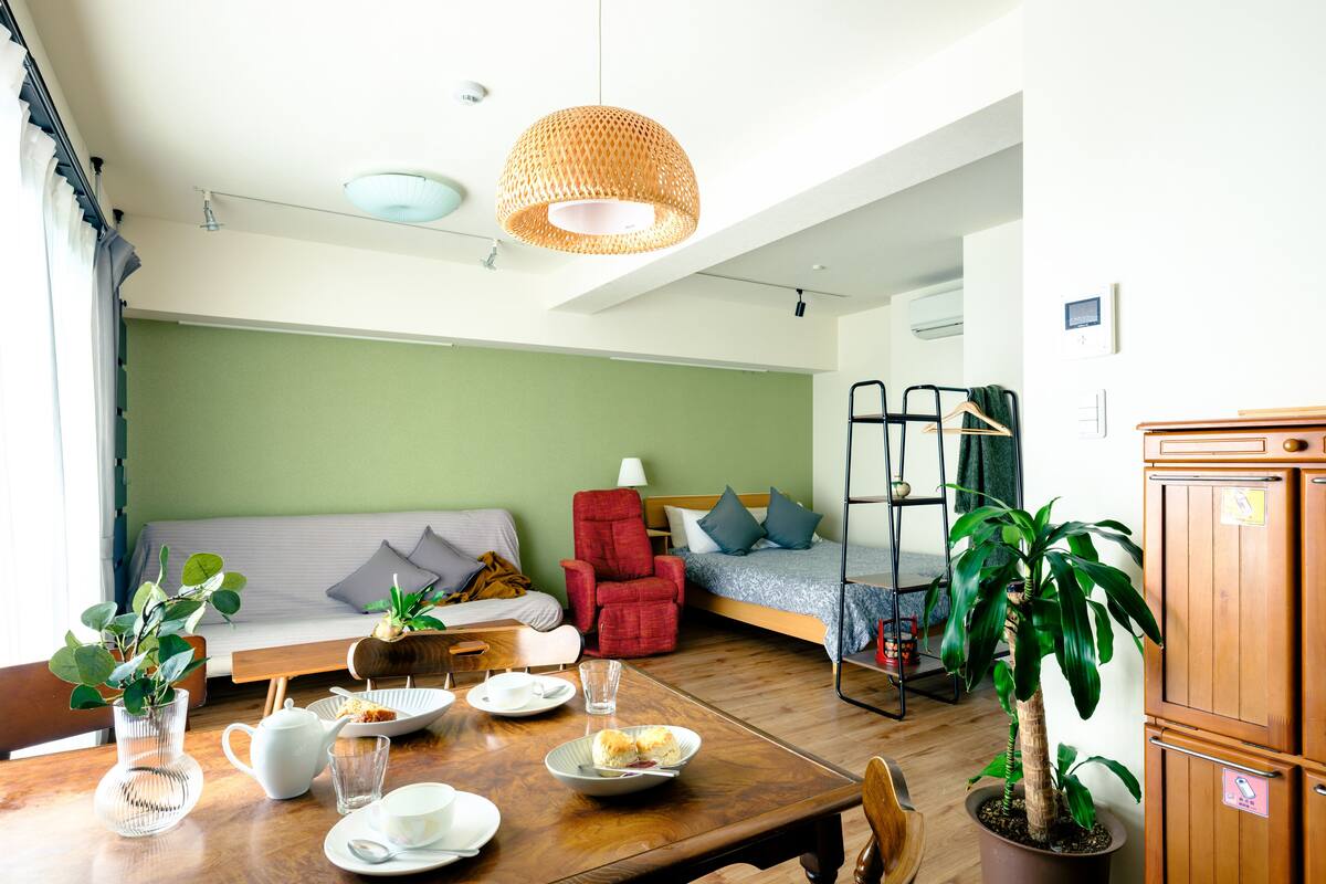 A modern living room with a wooden dining table set for a meal, a sofa, a red armchair, and a bunk bed in the background.