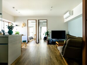 Ein modernes Wohnzimmer mit großem Flachbildfernseher, Holzboden, einer Couch und einem Essbereich mit Tisch und Stühlen.