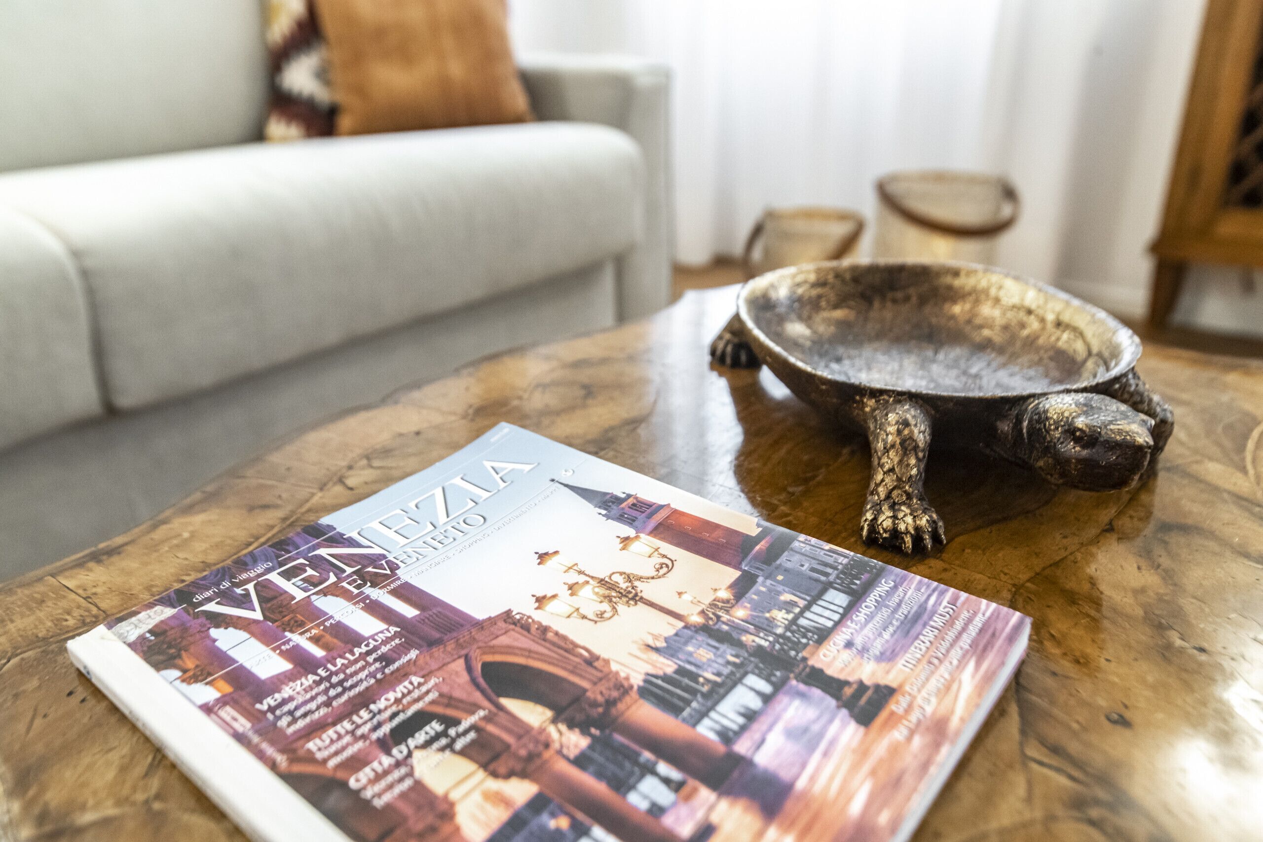 A magazine on a wooden coffee table with a decorative bowl and a sofa in the background.