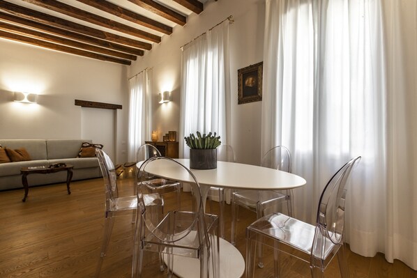 A dining area with a round table, clear chairs, and a potted plant.