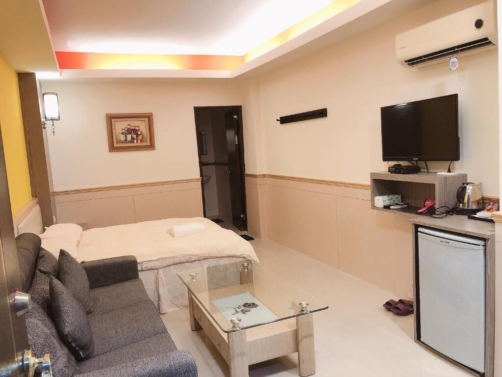 A compact hotel room with a bed, a sofa, a small coffee table, a television, a mini-fridge, and a microwave.
