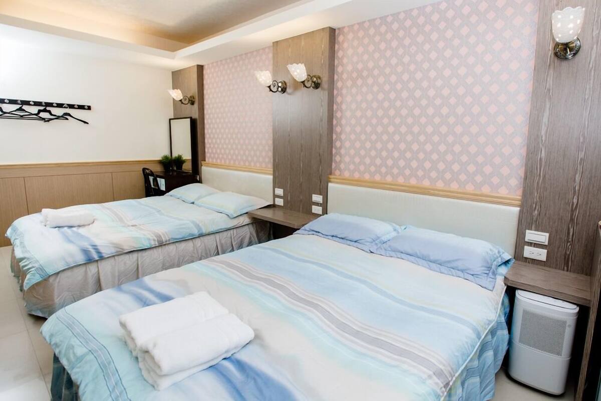 A hotel room with two beds, a mirror, a wall-mounted light fixture, and a small trash bin.