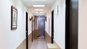 A long, narrow hallway with white walls and a tiled floor. There are several doors on the right side, and a bench in the center. - Taipei 101 Yurmans House (Taipei)