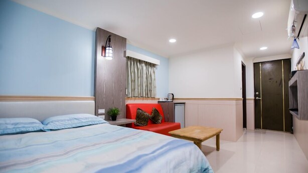 A bedroom with a bed, a red sofa, a small table, and a kitchenette area. - Taipei 101 Yurmans House (Taipei)