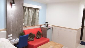 A compact room with a red sofa, a small wooden table, a kitchenette with a coffee maker, and a window with curtains. - Taipei 101 Yurmans House (Taipei)