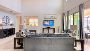 Een ruime woonkamer met een grijze bank, een televisie en een groot raam.