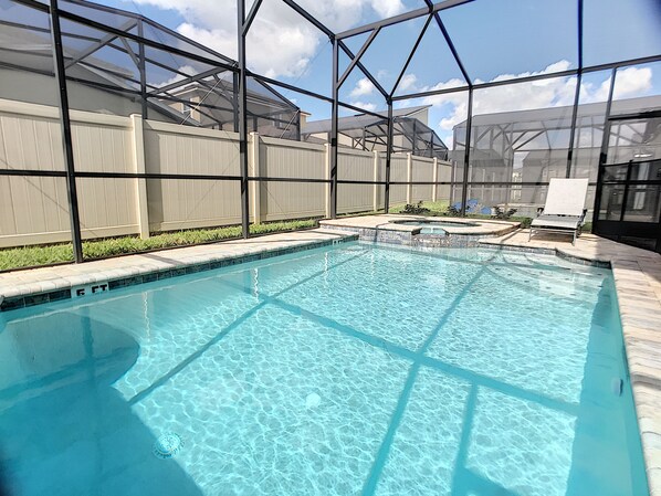 A rectangular swimming pool with clear blue water, surrounded by a glass enclosure and a white fence.