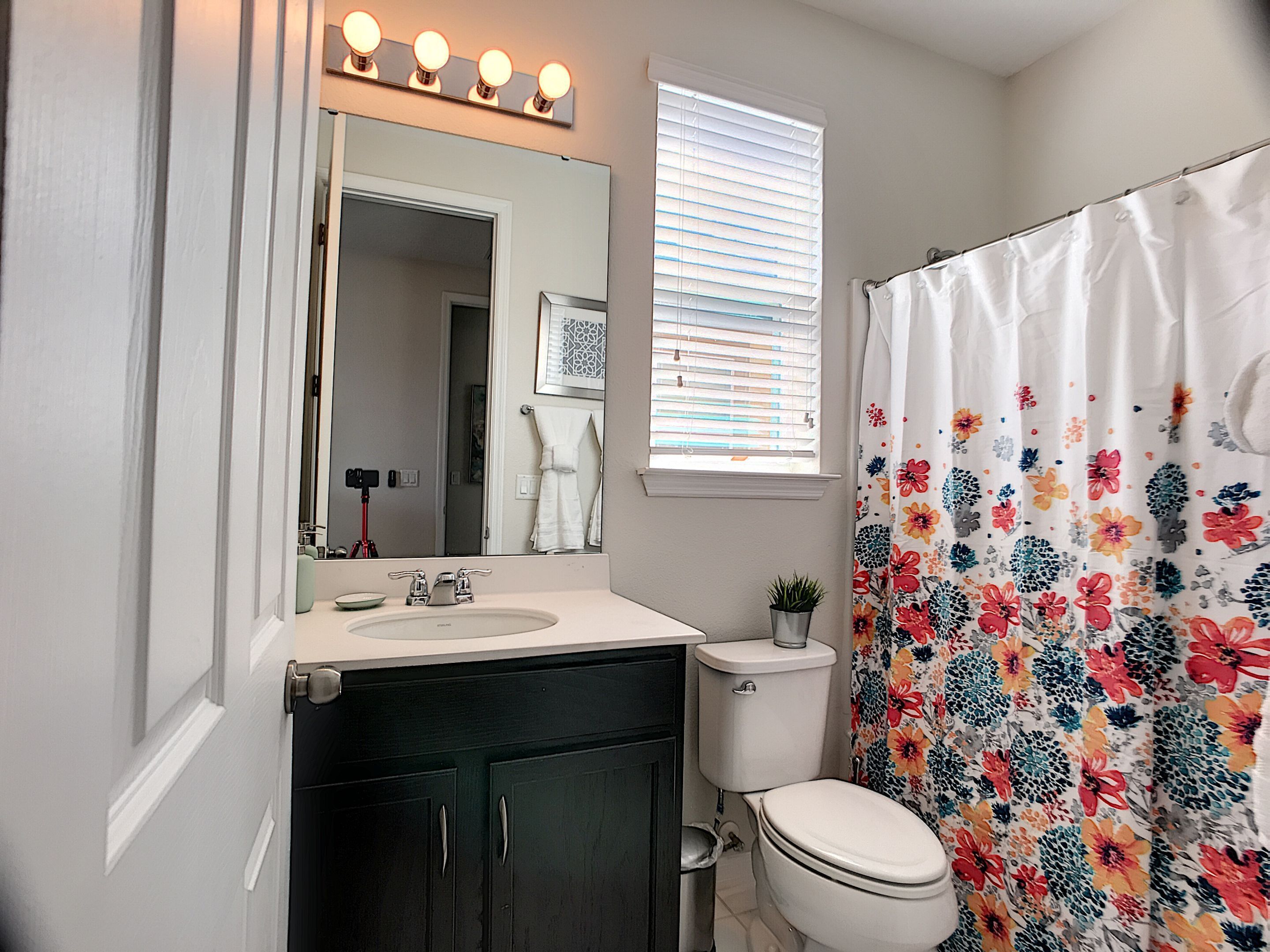 A bathroom with a white sink, dark cabinets, a toilet, and a shower curtain with a floral pattern.