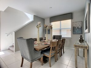 A dining area with a high ceiling, a staircase, and a window with blinds.