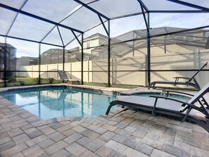 A swimming pool with a glass enclosure, surrounded by a brick patio and a white fence.