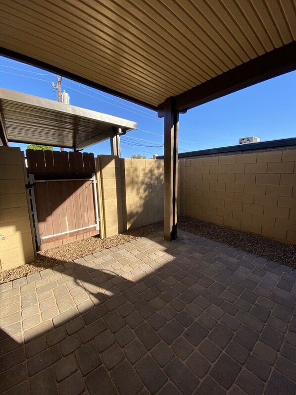 A covered patio area with a brick floor, a wooden fence, and a view of the sky.