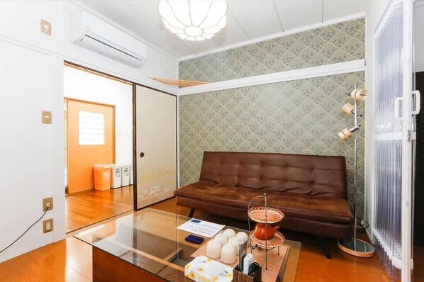 A modern living room with a brown leather sofa, a glass coffee table, and a decorative tea set. - Nishi shinjyuku wa-an homestay (Tokyo)