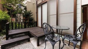 Un petit patio extérieur avec un banc en bois, deux chaises en métal et une table.