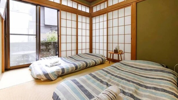 Une pièce de style japonais traditionnel, avec un sol recouvert de tatamis, des portes coulissantes et un lit avec une literie à rayures.