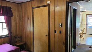 Una habitación con paneles de madera, ventilador de techo, puerta con cerradura de tarjeta y ventana con cortinas.