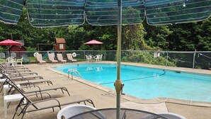 Un área de piscina con sillones de descanso, sombrillas y una mesa.