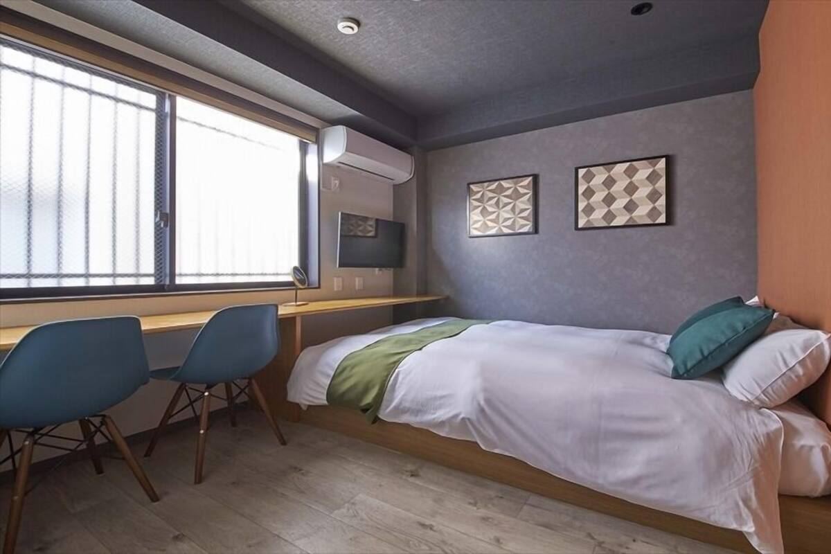 A compact room with a bed, a desk, two chairs, and a window.