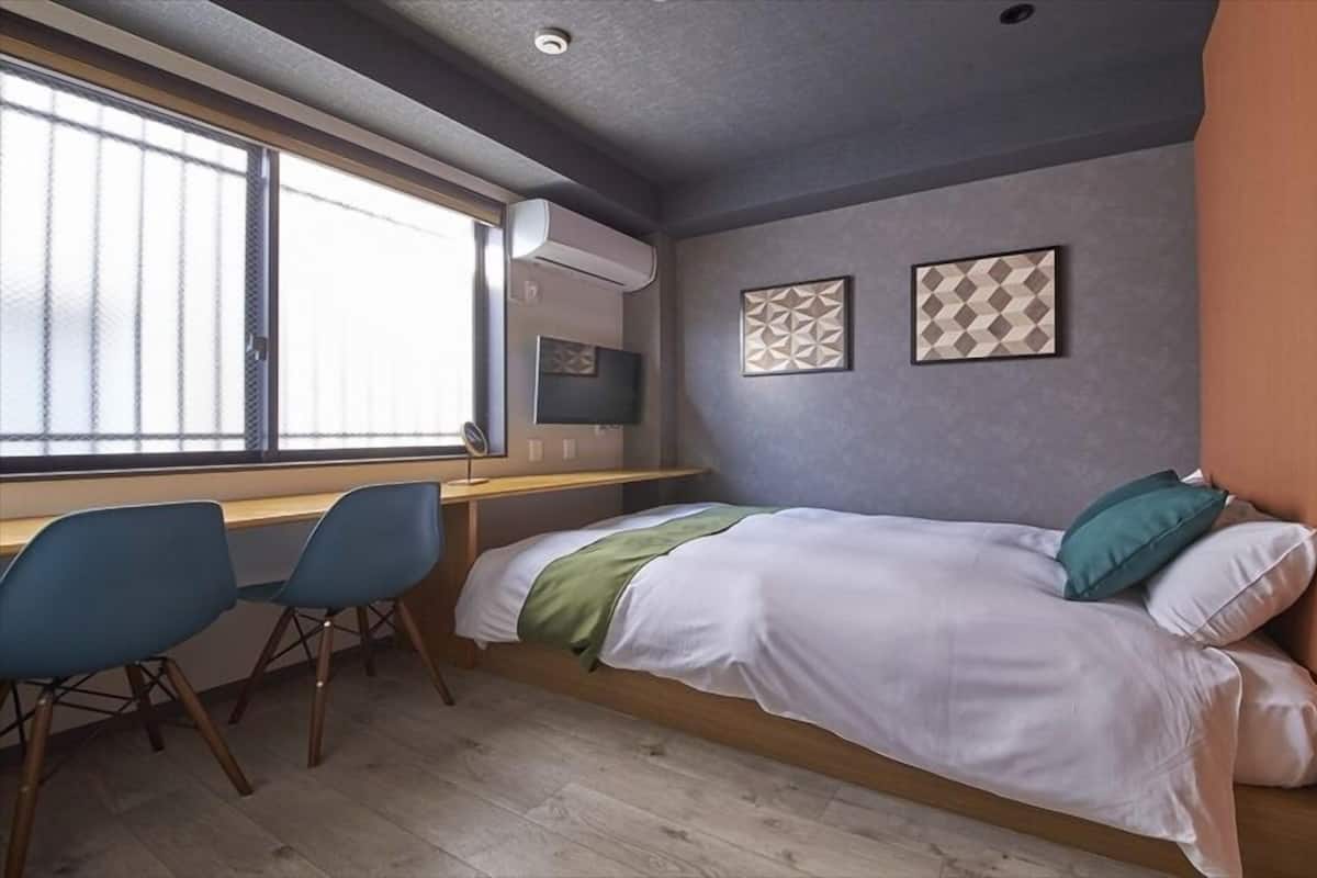 A compact room with a bed, a desk, two chairs, and a window.