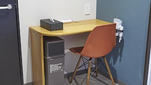Un petit espace de travail compact, avec un bureau en bois, une poubelle et une seule chaise orange.