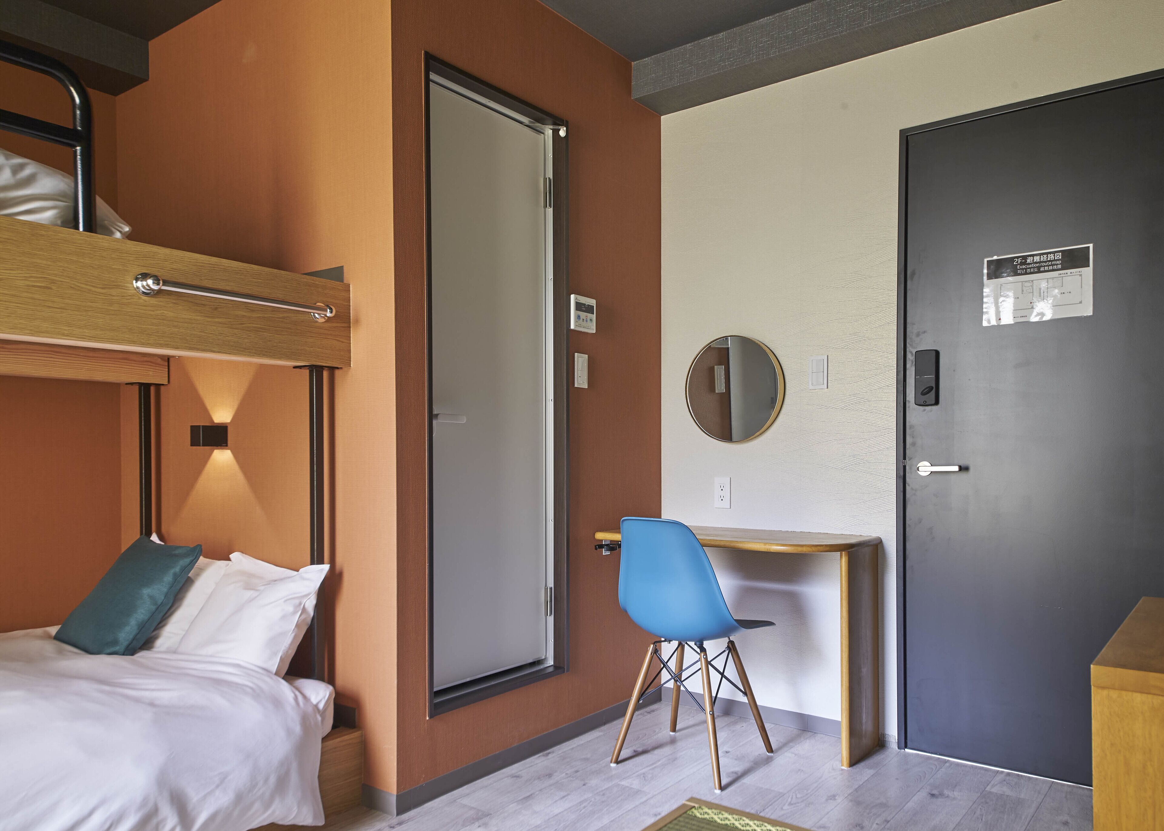A hotel room with a bunk bed, a desk, a chair, and a door with a sign.