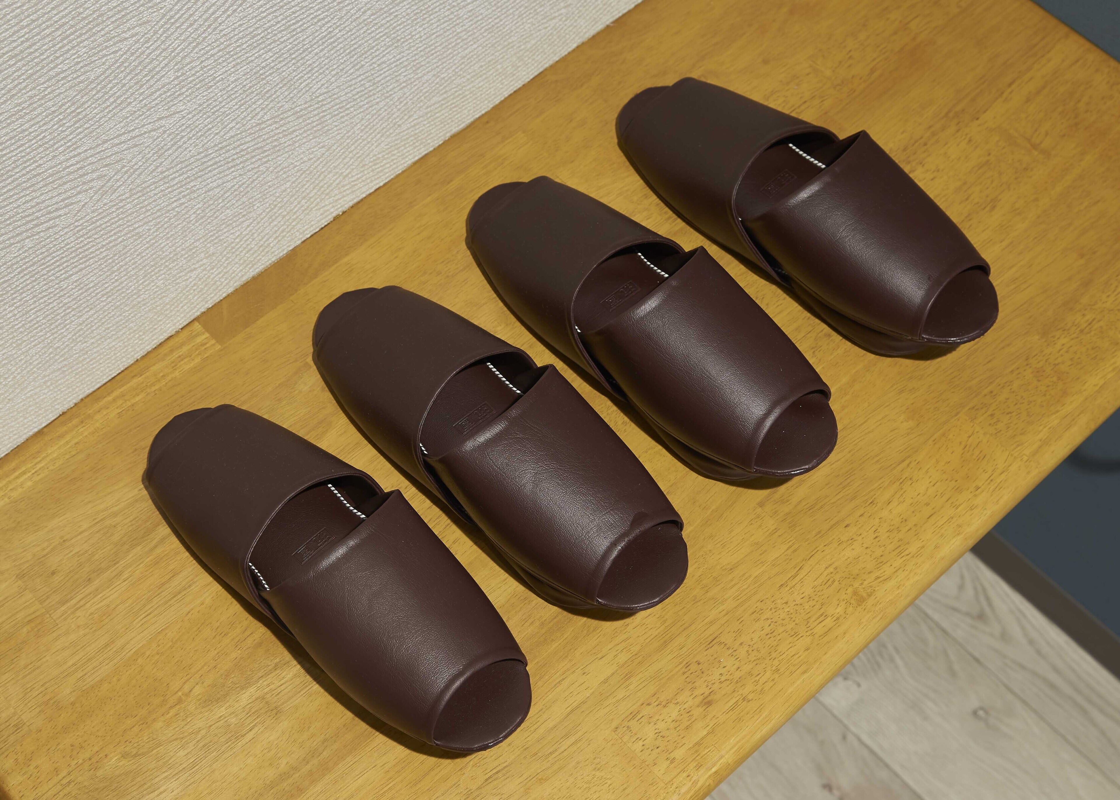 Four brown leather slippers on a wooden table.