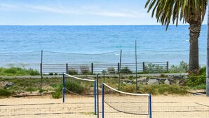 Una cancha de voleibol de playa con red, rodeada por una valla y palmeras, con vista al océano.
