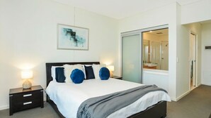 Una habitación de hotel moderna con una cama, mesitas de noche, un cuadro y una puerta corredera hacia el baño.