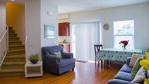 Una sala de estar con una escalera, un comedor con mesa y sillas, y una cocina con armarios.