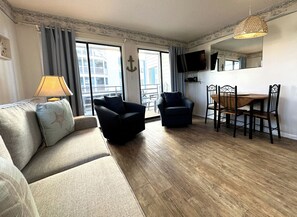 Relax in this stylish living room with a sofa, armchair, and dining table, featuring a flat-screen TV and large windows with an outside view.