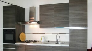 A modern kitchen with dark wood cabinets, a stainless steel sink, and a gas stove. - Cosy apartment for 4 people with WIFI, TV and patio (Imperia)