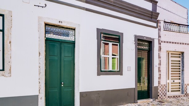 A building with two green doors and a window, a tiled ground, and a brick wall. - TREM HOUSE - LOCATED IN OLD CITY - FARO (Faro)
