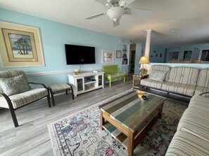 A living room with a television, striped sofas, a green chair, and a patterned rug.