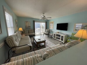 A living room with striped sofas, a coffee table, a TV, and a ceiling fan.
