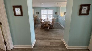A dining area with a wooden table and chairs, light blue walls, and a window with blinds. - Come On In (Downstairs) - Second Row in Garden City Beach (Garden City Beach)