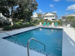 Une piscine avec un escalier en métal, entourée de chaises longues et d’une clôture.