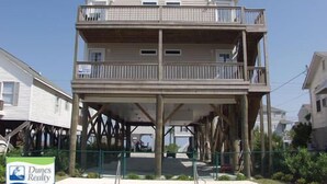 A two-story building with a balcony on the upper floor, a covered area below, and a swimming pool in front. - Come On In (Downstairs) - Second Row in Garden City Beach (Garden City Beach)