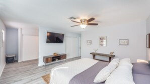 A bedroom with a bed, a ceiling fan, a TV mounted on the wall, and a small wooden table. - Charming & Stylish home can accommodate 8 guests! (Henderson)