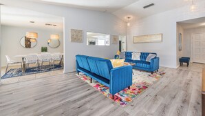 A modern living room with a blue sofa, a dining area with a white table and chairs, and a colorful rug. - Charming & Stylish home can accommodate 8 guests! (Henderson)