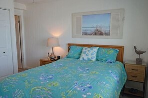 A bedroom with a bed, a nightstand, a lamp, a framed picture on the wall, and a small shelf with a bird figurine. - Beach House 315 - Oceanfront in Garden City Beach (Garden City)