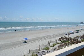 A beach with a wooden boardwalk, umbrellas, and a pier in the background. - Beach House 315 - Oceanfront in Garden City Beach (Garden City)