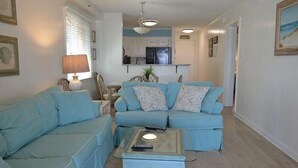 Una sala de estar con un sofá azul, una mesa de centro y una cocina al fondo.