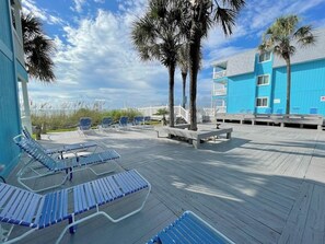 A wooden deck with lounge chairs, palm trees, and a building with blue siding. - Beach House 315 - Oceanfront in Garden City Beach (Garden City)