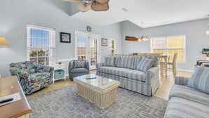 A spacious living room with a large sofa, a coffee table, and a dining area with a table and chairs. - Southern Faire - Second Row in Surfside Beach (Surfside Beach)