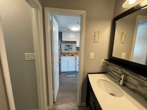 A modern bathroom with a large mirror, a sink, and a doorway leading to a kitchen area. - Carolina Shores II 2206 - Oceanfront Complex (Oceanview Unit) in Garden City Beach (Garden City)