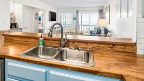 A modern kitchen with a wooden countertop, stainless steel sink, and blue cabinets. - Captain's Walk III 1C - Oceanfront in Garden City Beach (Garden City)