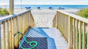 A wooden boardwalk leading to a beach with blue umbrellas and lounge chairs. - Captain's Walk III 1C - Oceanfront in Garden City Beach (Garden City)